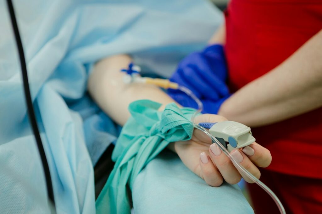 Nurse monitors a seated adult receiving clear IV fluids through a catheter in the arm.